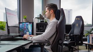 A man sits at a desk on a Secretlab chair.