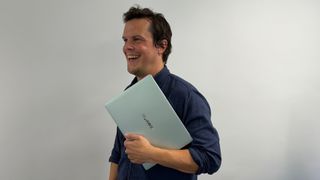 A smiling man holds a green laptop, because it makes him happy.