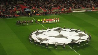 Photo of a football pitch with dozens of people spreading out a canvas showing the Champions League Starball