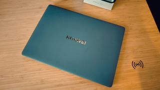 A blue Huawei Matebook X Pro laptop on a wooden desk, in front of blue and orange LED lights.