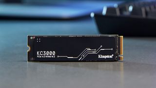 Photograph of Kingston KC3000 solid state drive on grey work surface with keyboard blurred and visible in background