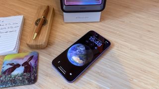 An ultramarine blue iPhone 16 on a wooden desk