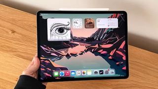 Hand holding an iPad Pro M2 over a wooden desk