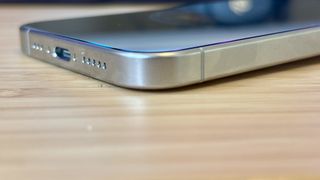 A grey titanium iPhone 15 Pro camera phone on a wooden desk